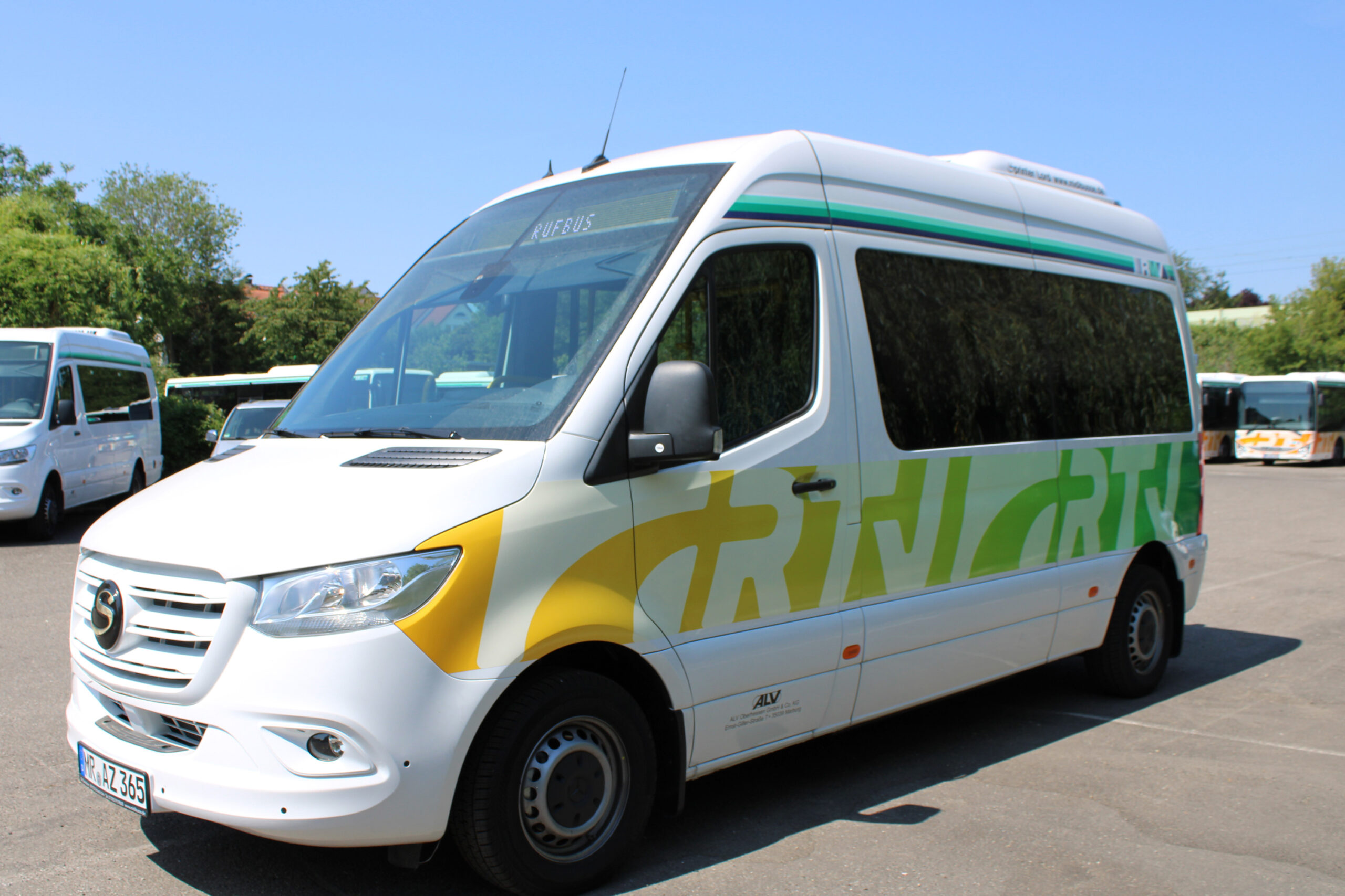 Ein weißer Rufbus der Rheingau-Taunus-Verkehrsgesellschaft mit grün-gelber „RTV“-Beklebung steht auf einem Parkplatz. In der Frontscheibe ist das Ziel „Rufbus“ angezeigt. Im Hintergrund sind weitere Kleinbusse geparkt.